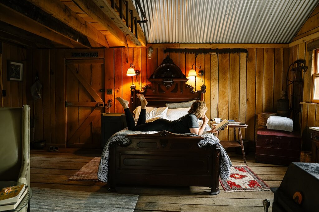 A self-portrait taken by Marybeth Wells of her laying across a bed reading inside of a Hipcamp Cabin near Woodstock, Virginia
