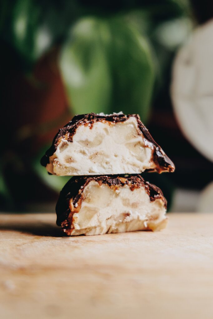 A Frozen Almond Butter Banana Bite cut in half and stacked, sitting on a wooden cutting board with a house plant in the background